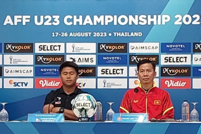 A coach and player at the AFF U23 Championship 2023 press conference backdrop with the official match ball on the table